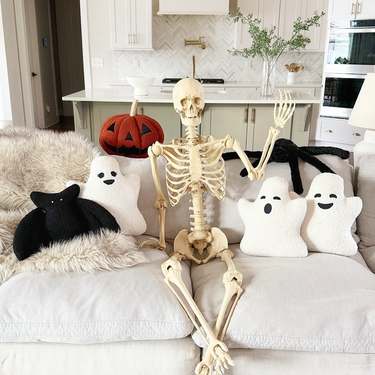 Halloween themed pillows on couch with large skeleton waving